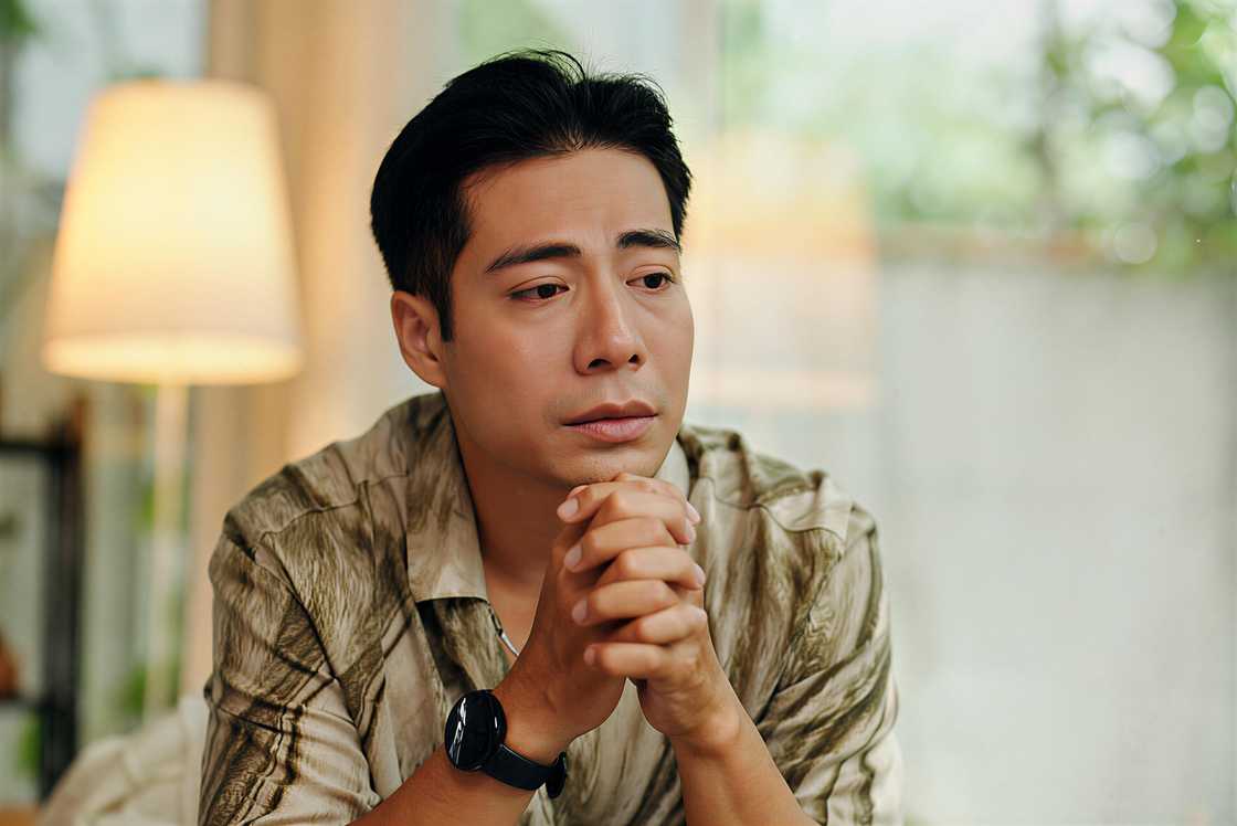An Asian man is sitting with a sad expression