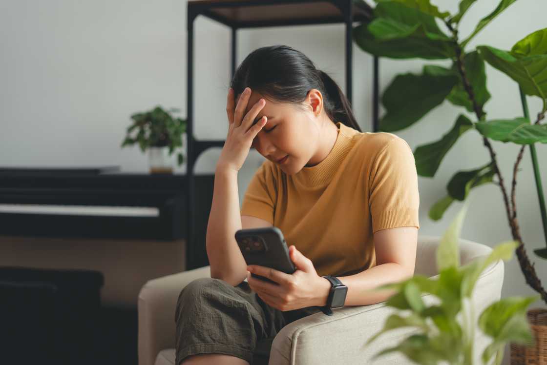 A sad woman sitting at home looking at her smartphone A sad woman sitting at home looking at her smartphone