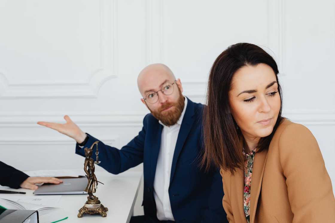 A man gestures in frustration while a woman turns away from him at a desk. A man gestures in frustration while a woman turns away from him at a desk.