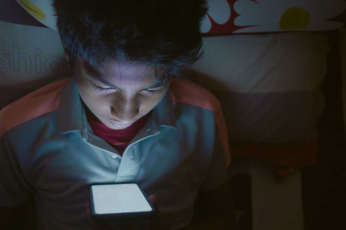 A young boy uses a smartphone in a dark room. A young boy uses a smartphone in a dark room.
