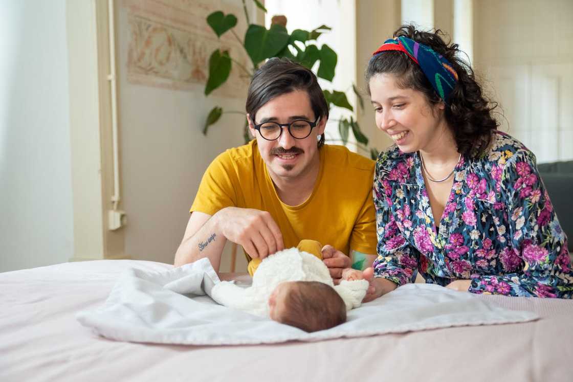 A couple smiles while gently caring for their newborn on a bed at home. A couple smiles while gently caring for their newborn on a bed at home.