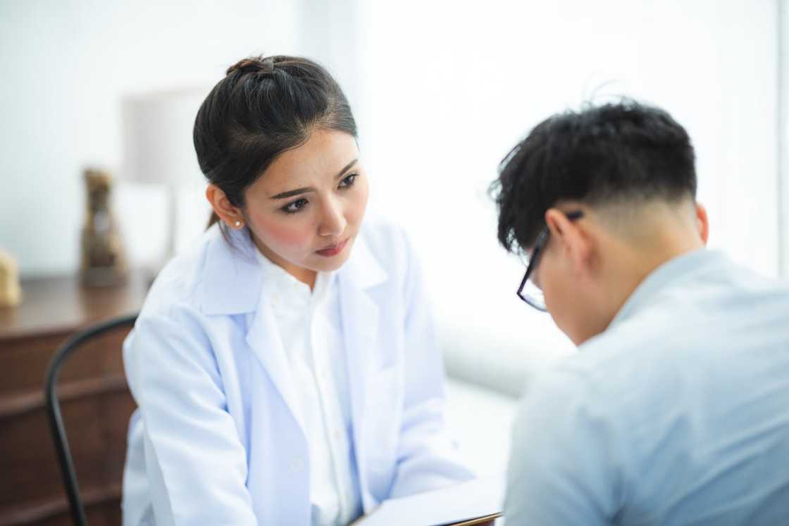 A doctor in a white coat listening attentively to a seated patient during a consultation. A doctor in a white coat listening attentively to a seated patient during a consultation.