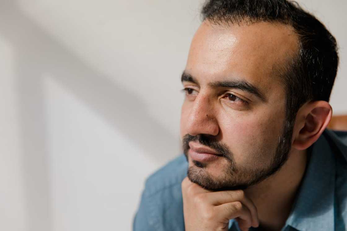 A thoughtful man rests his chin on his hand while looking into the distance.