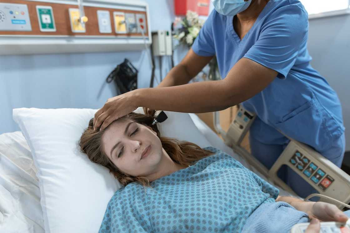 A nurse checks a woman lying in a hospital bed during a medical examination.