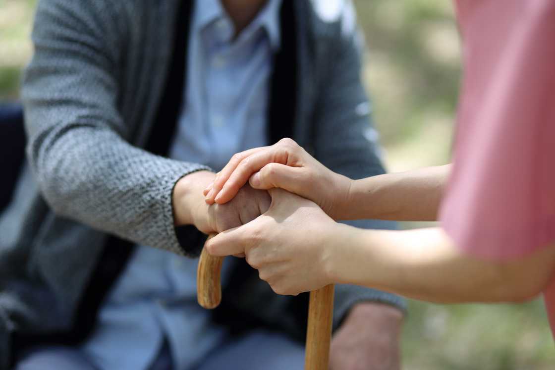 A lady holds the hand of a man who is using a walking stick