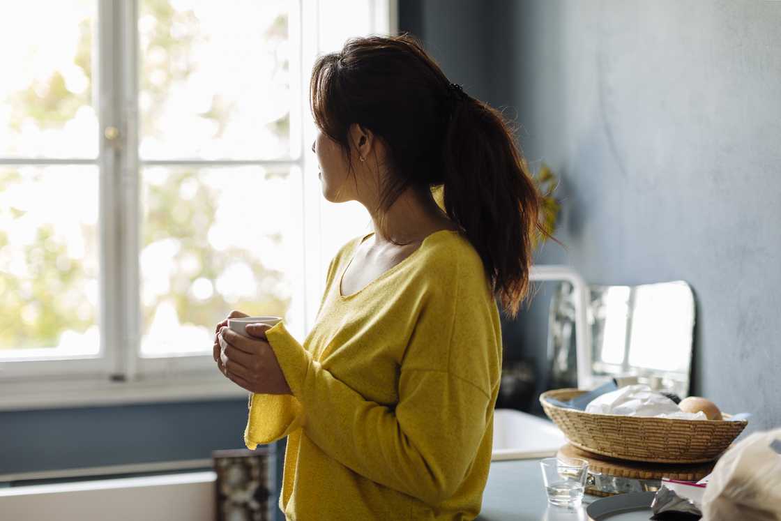 A lady looking outside the window with a cup of tea