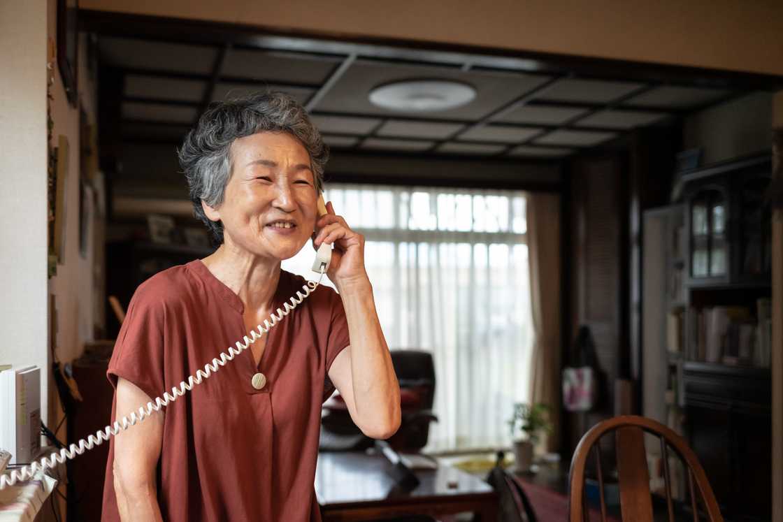 A senior Japanese woman is talking on a landline A senior Japanese woman is talking on a landline