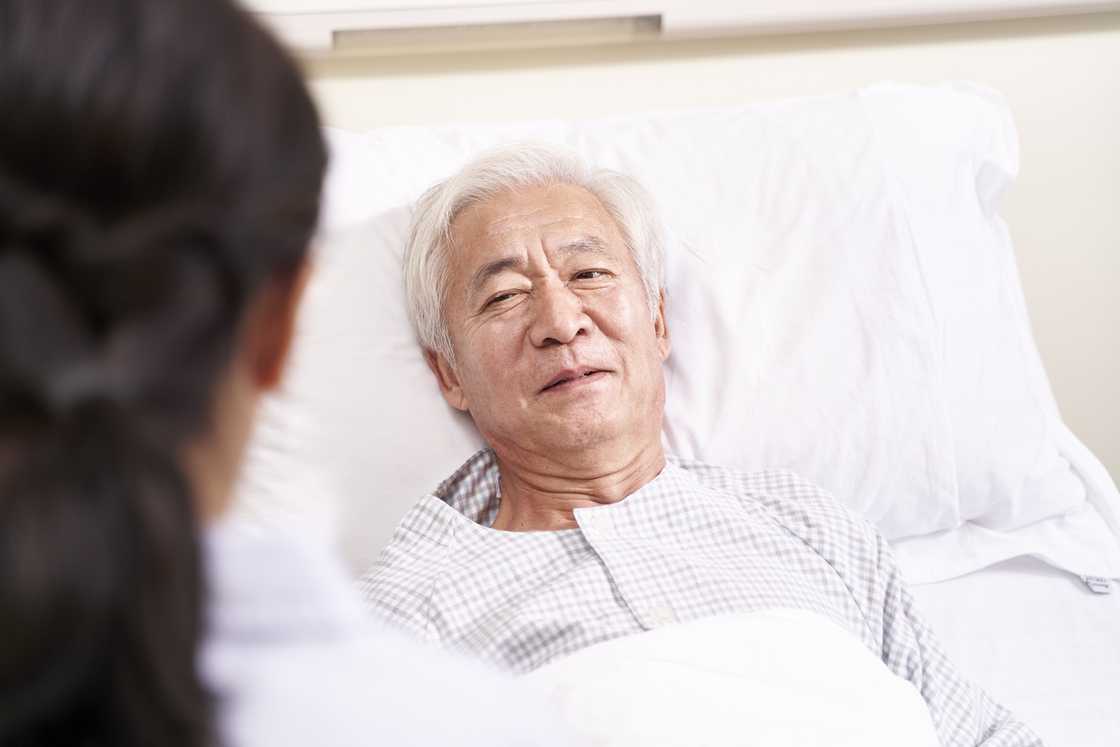 An Asian old man lying in a hospital bed, appearing unwell