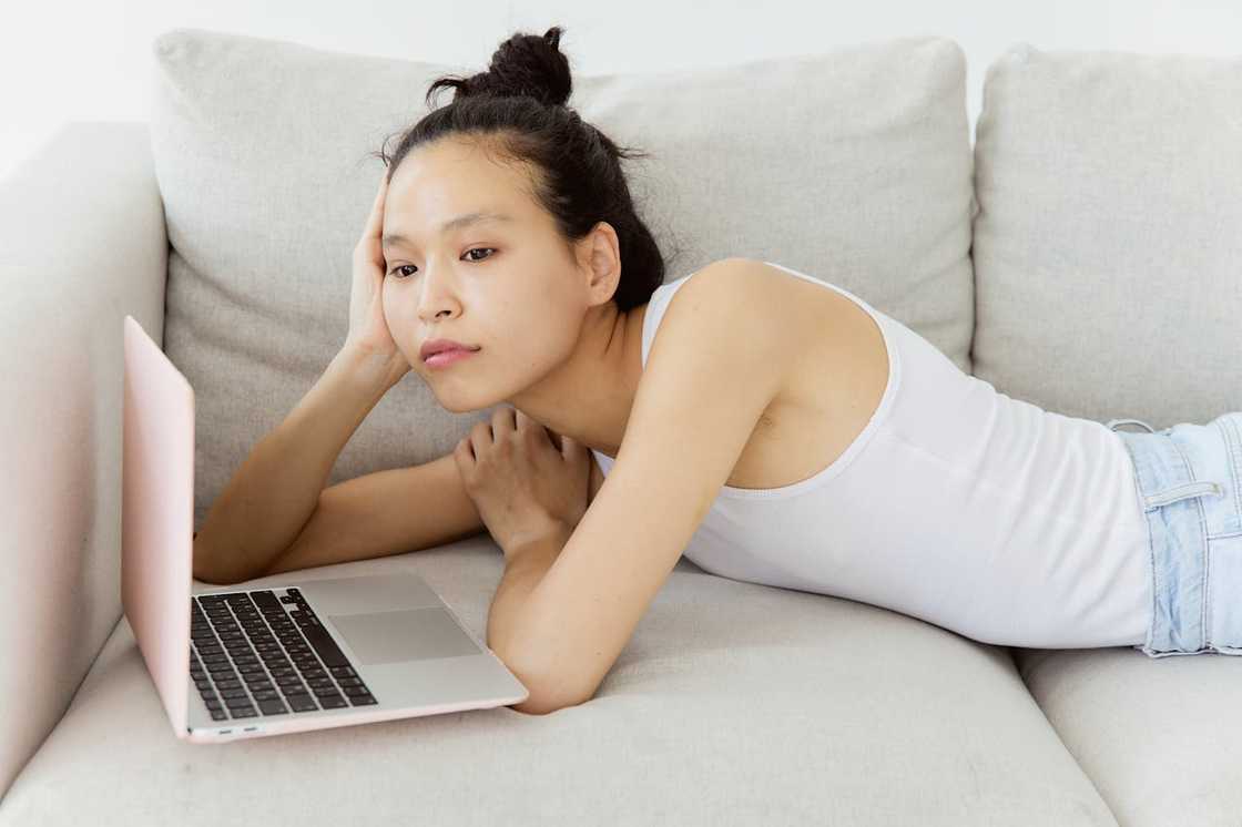 A person in a white tank top and denim shorts lies on a couch.