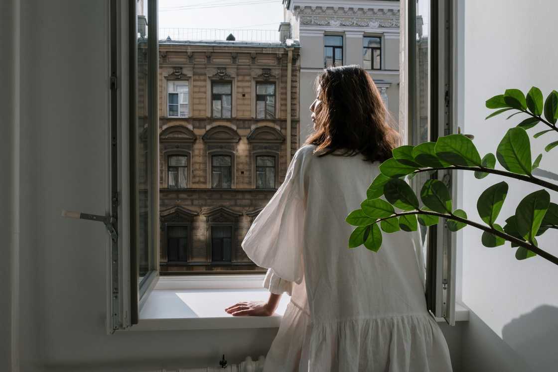 A thoughtfull woman standing on the window in the morning