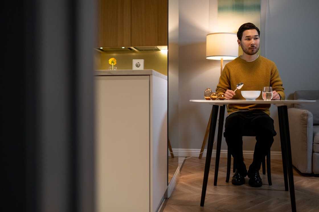 A man sits alone at a small dining table with a bowl of food.