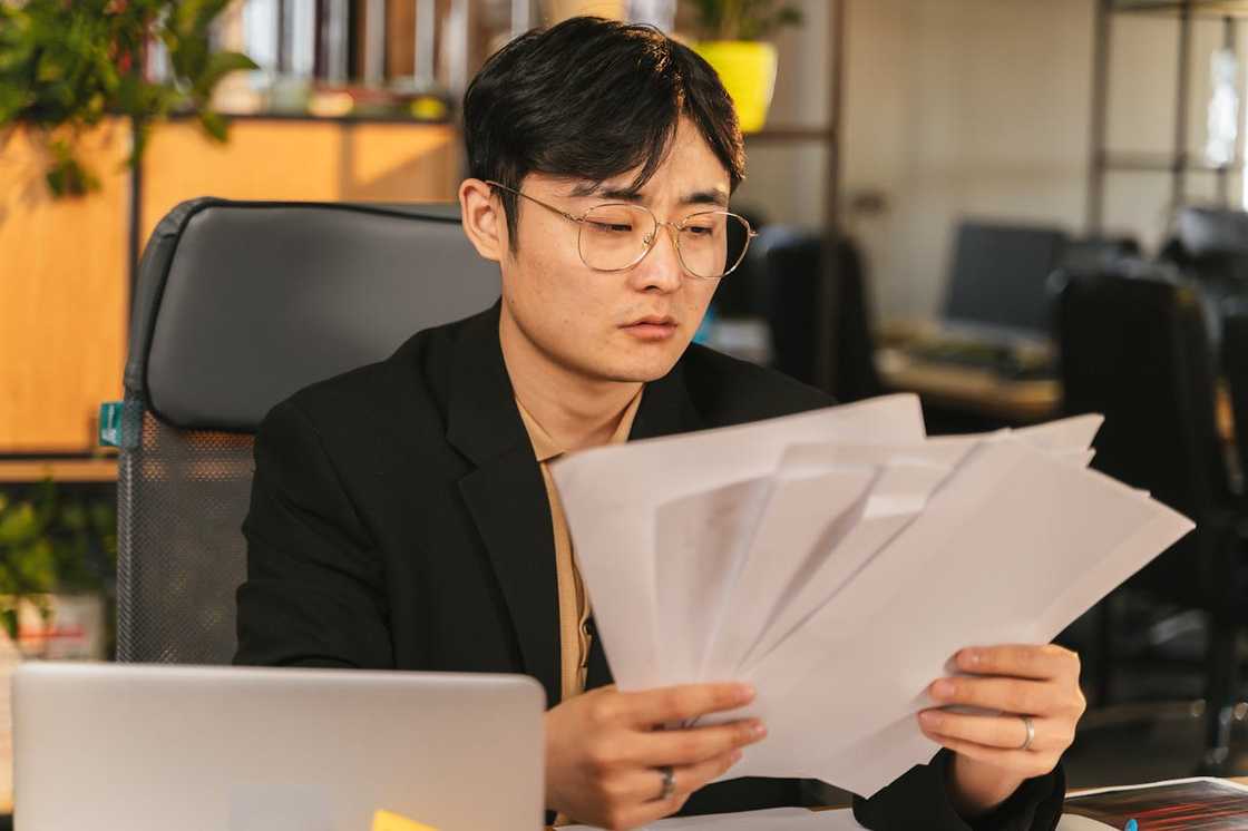 An office worker reviewing multiple documents at a desk, looking concerned. An office worker reviewing multiple documents at a desk, looking concerned.
