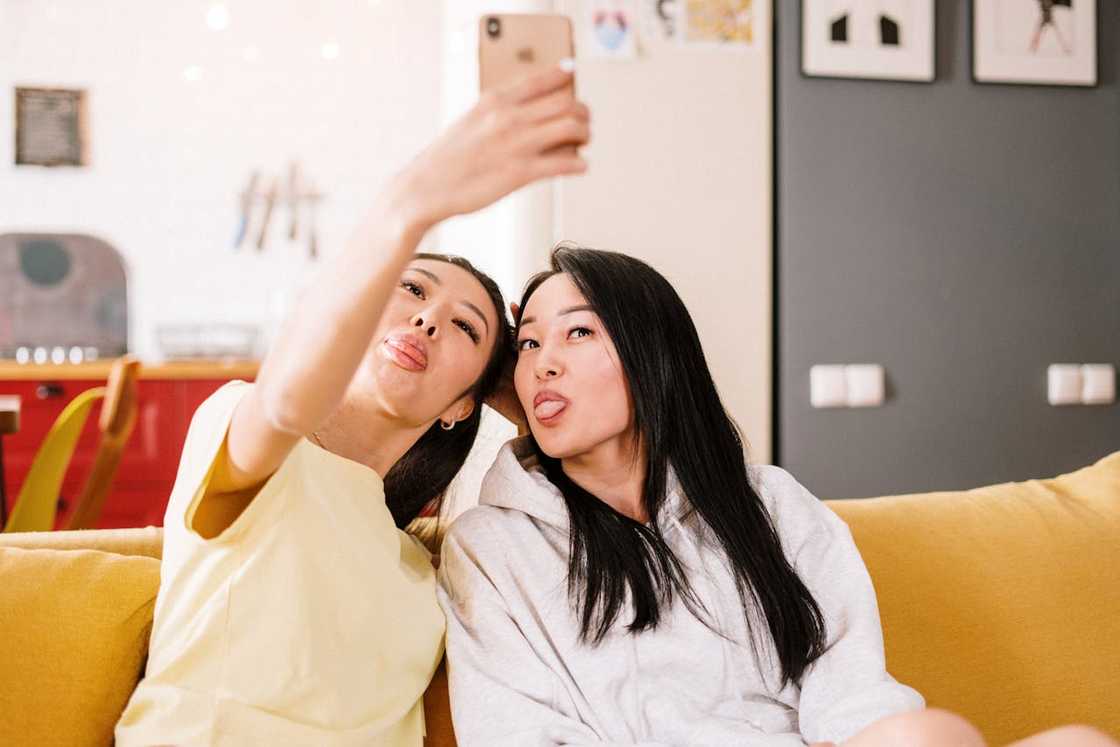 Two young women take a selfie sitting on a couch. Two young women take a selfie sitting on a couch.