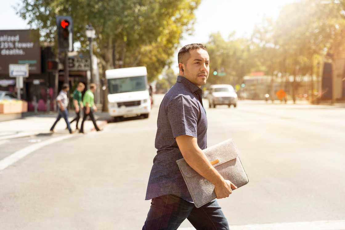 A man crosses a street holding a folder. A man crosses a street holding a folder.