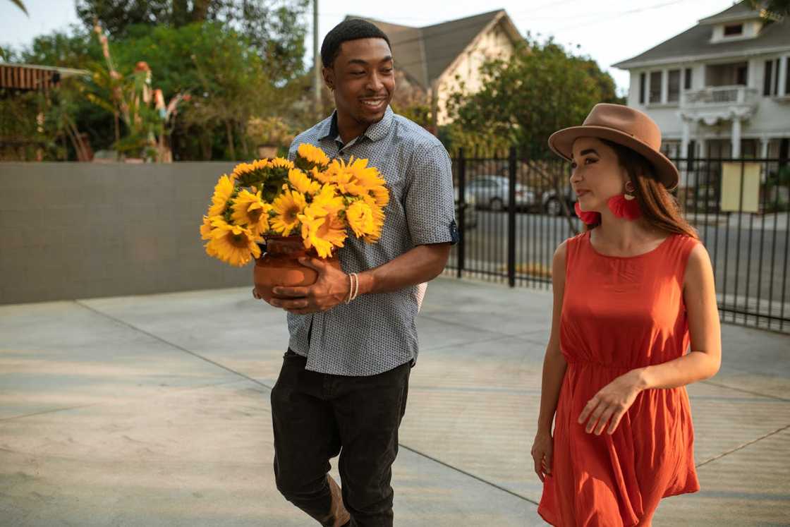 Man carrying a pot of sunflowers while walking beside a woman. Man carrying a pot of sunflowers while walking beside a woman.