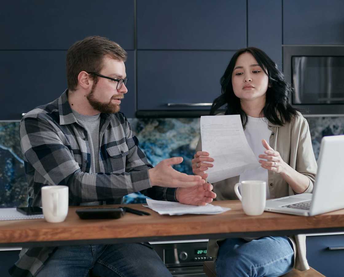 A couple converses over some documents together at a wooden table.