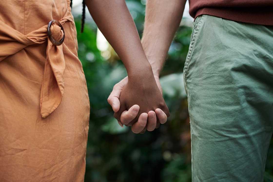 A couple hold hands while standing outdoors.