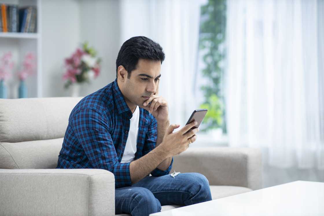 A man staring at his phone while sitting on his couch