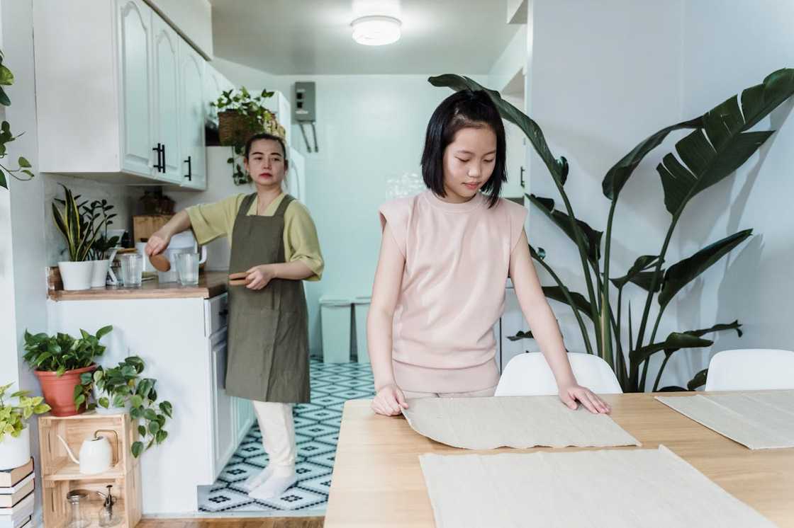 A daughter ignores her mother as she prepares the dining table. A daughter ignores her mother as she prepares the dining table.