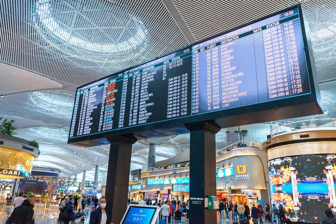 Travellers crowd around TV screen showing flight data.