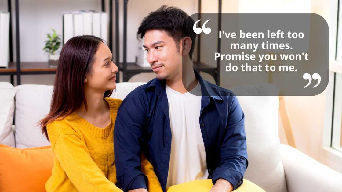 A young couple hold hands sitting on sofa looking affectionate