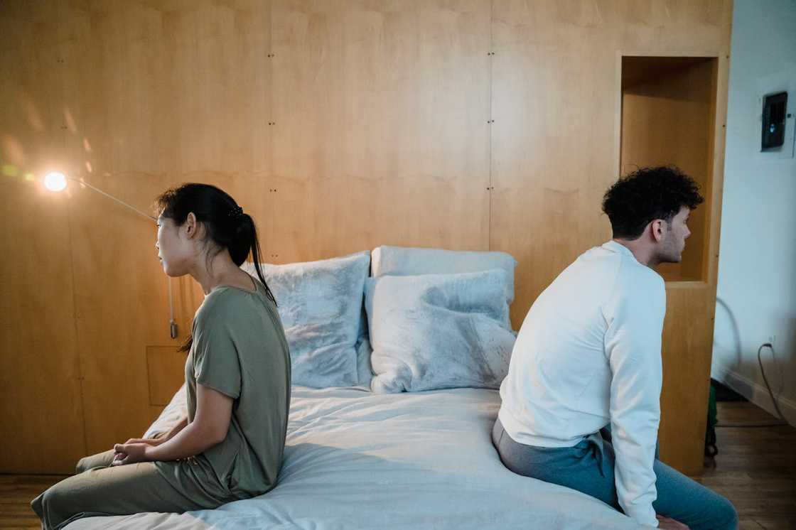 A couple sitting back-to-back on a bed, facing away from each other after an argument. A couple sitting back-to-back on a bed, facing away from each other after an argument.