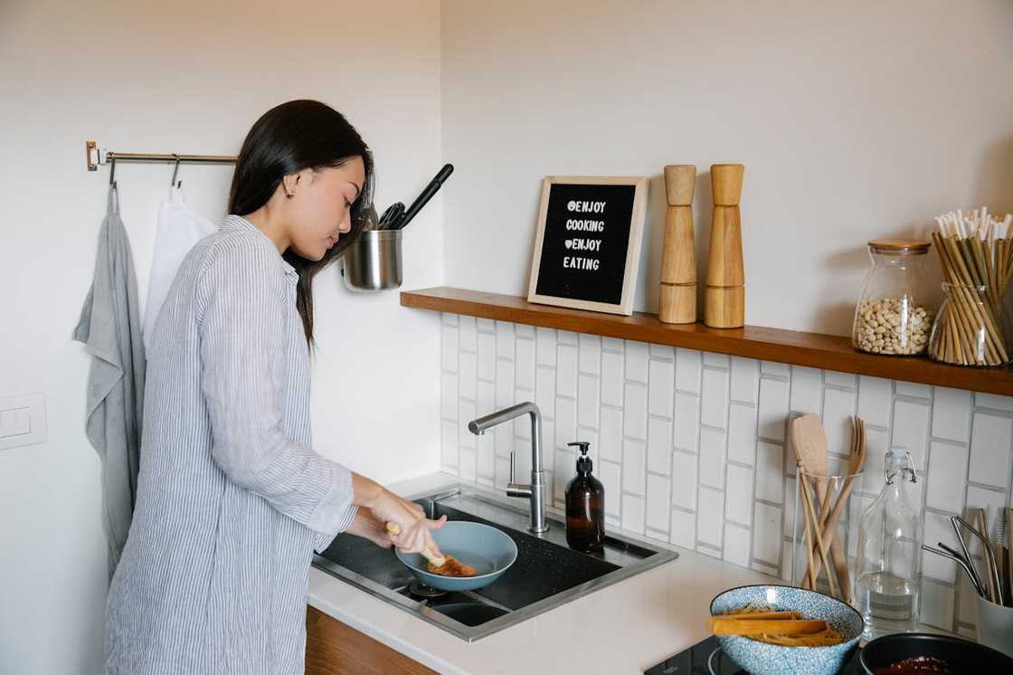 An Asian woman washes the dishes at home.