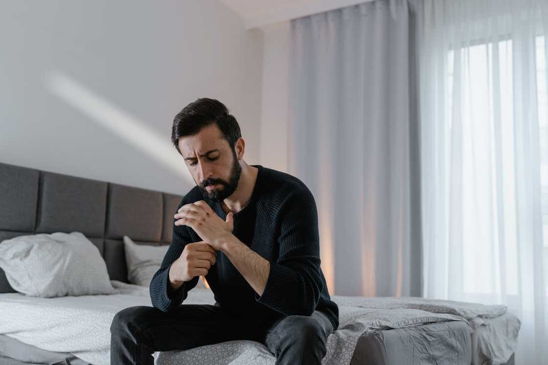 A man sits on the edge of a bed, looking worried and deep in thought. A man sits on the edge of a bed, looking worried and deep in thought.