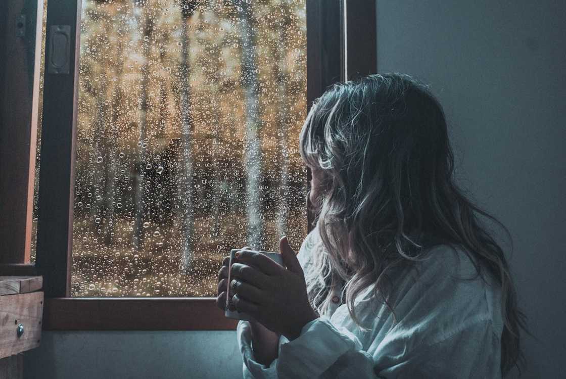 A woman looks out through a rain-covered window with a distant expression. A woman looks out through a rain-covered window with a distant expression.
