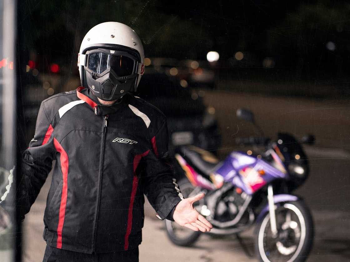 Motorbike rider wearing helmet and mask beside parked bike.