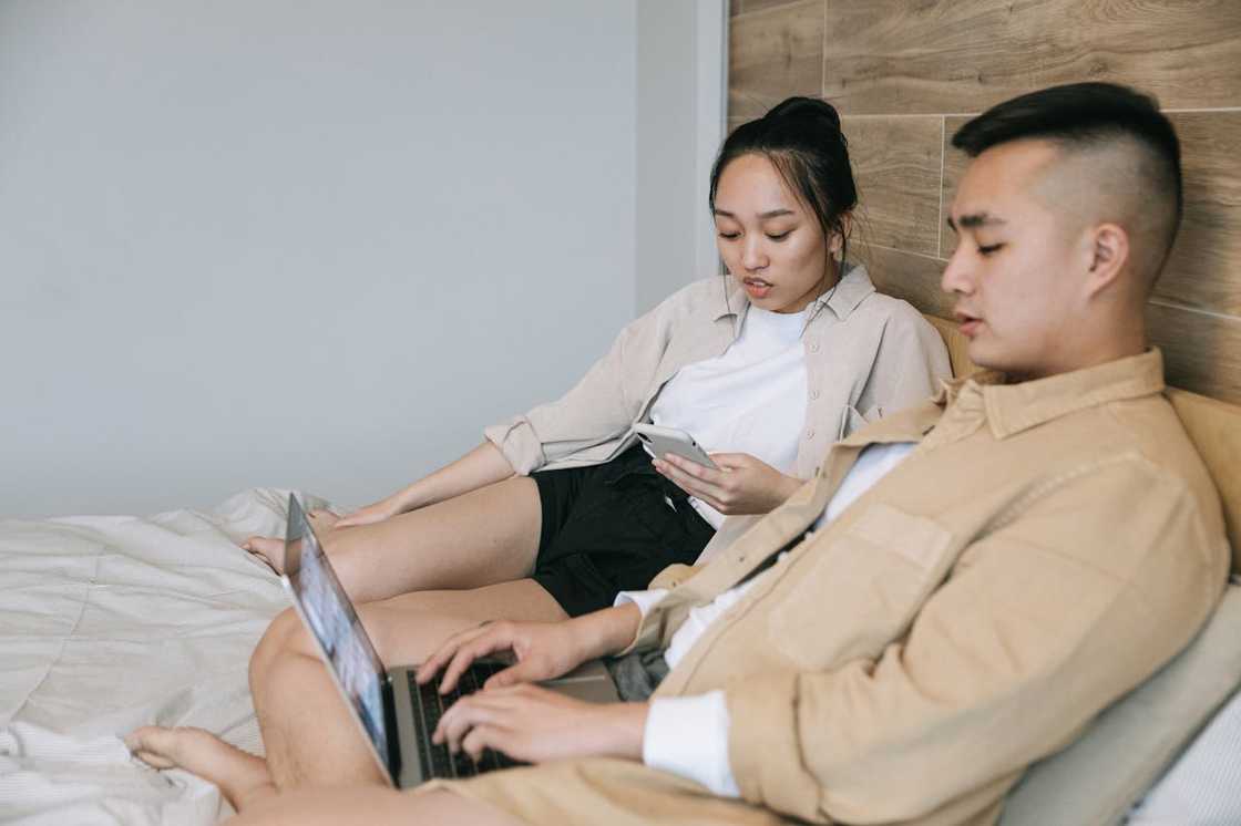 An Asian couple does research on something on their respective devices.