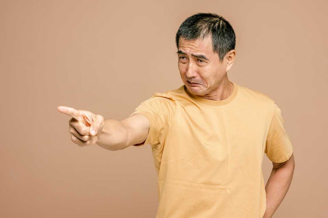 A man in a yellow shirt points forward with an upset, angry expression.
