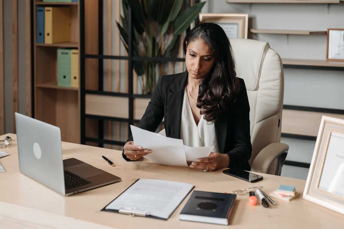 A woman works at a desk with a laptop and documents.