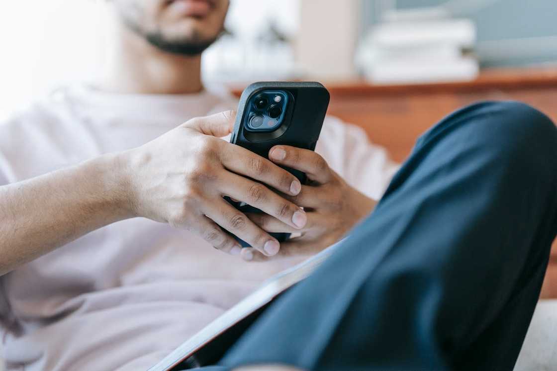 A man sits indoors, holding and looking at a smartphone.