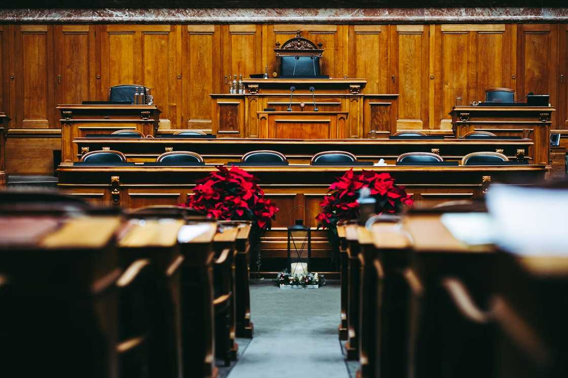 Interior of a formal chamber with wooden desks, central podium, microphones, and red poinsettias. Interior of a formal chamber with wooden desks, central podium, microphones, and red poinsettias.