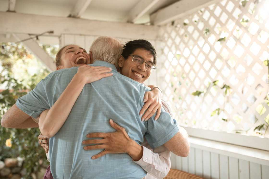 Three people share a joyful group hug on a porch.