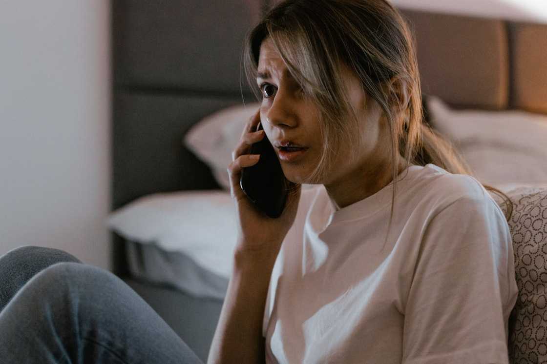 Worried woman sitting on a bed, talking on a phone.