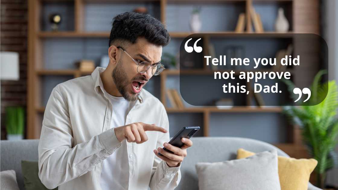 An angry young man pointing at his smartphone while sitting at home An angry young man pointing at his smartphone while sitting at home