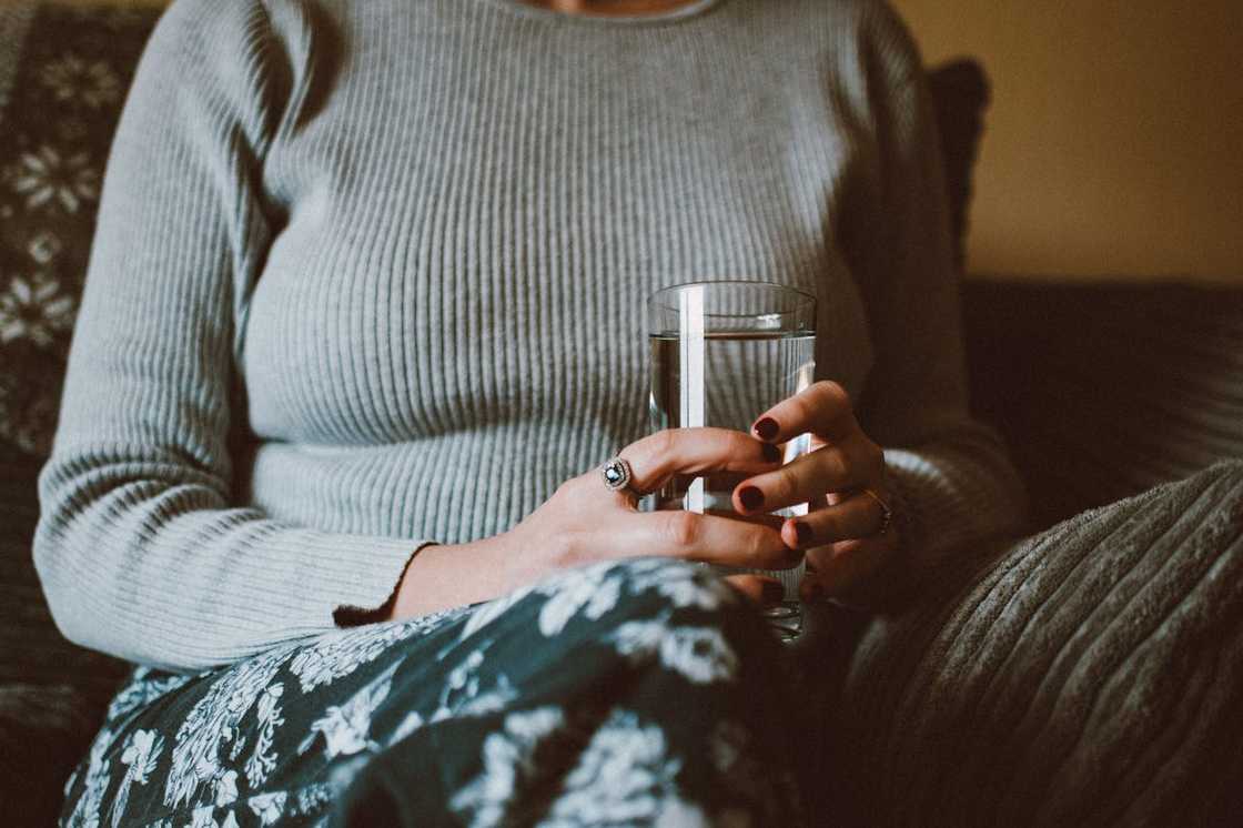 A woman sits holding a glass of water, looking thoughtful. A woman sits holding a glass of water, looking thoughtful.