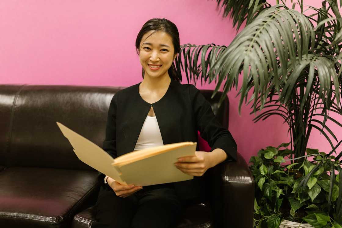 A woman sitting on a black leather couch while holding a folder. A woman sitting on a black leather couch while holding a folder.