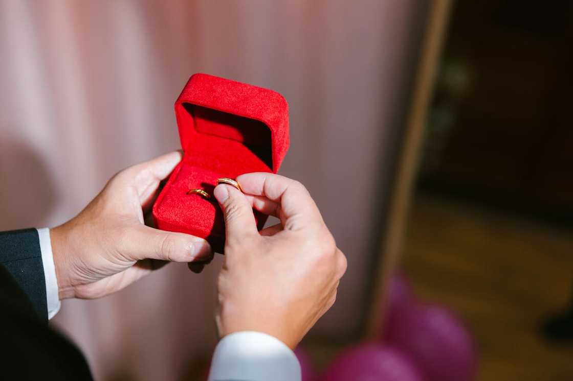 A person holds an open ring box displaying a gold ring. A person holds an open ring box displaying a gold ring.