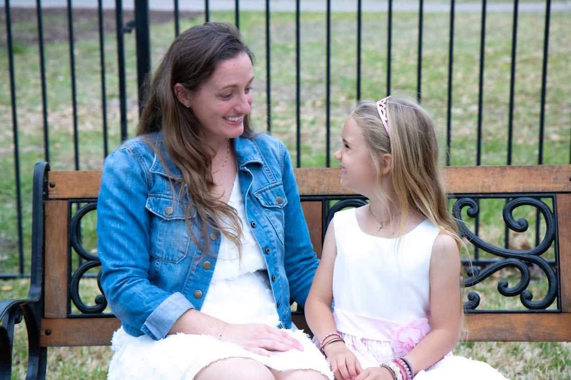 A woman and young child smiling together on a park bench.