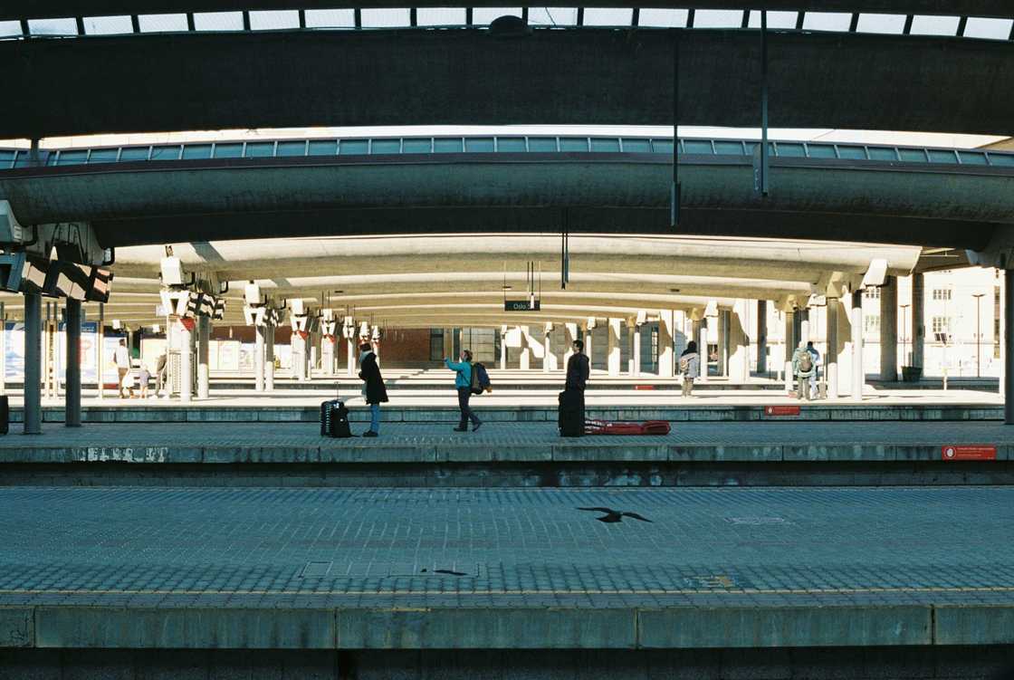 Train station platform with people, luggage, and modern concrete architecture.