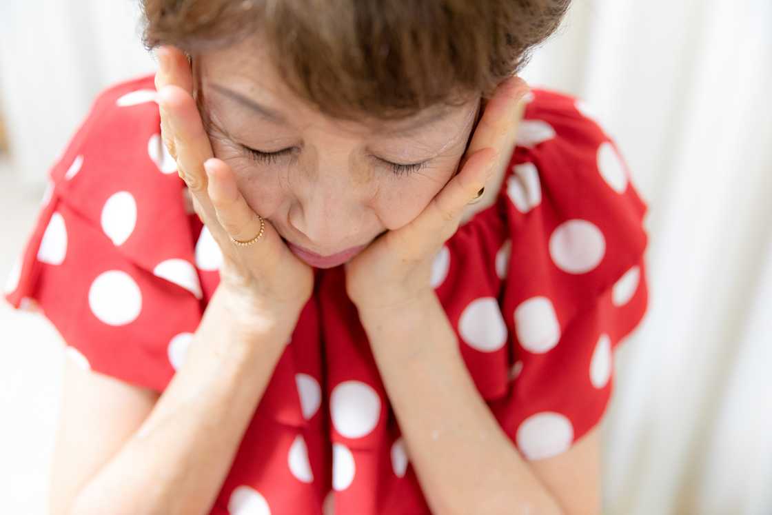 A helpless senior woman holding her cheeks A helpless senior woman holding her cheeks
