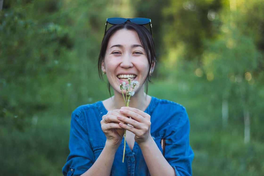 A smiling woman outdoors holding small wildflowers.