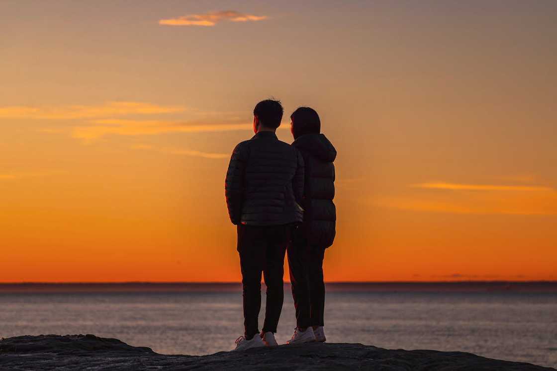 Two people sit at a stone picnic table during sunset. Two people sit at a stone picnic table during sunset.