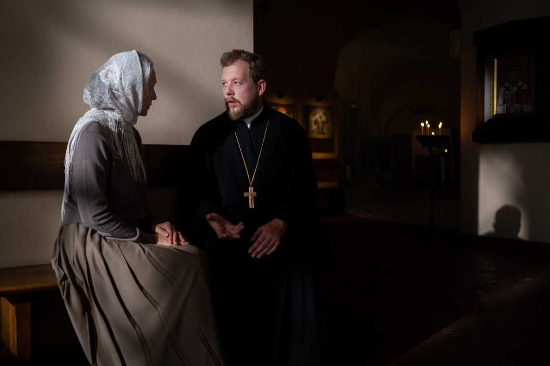 A priest listens as a woman speaks quietly inside a church. A priest listens as a woman speaks quietly inside a church.