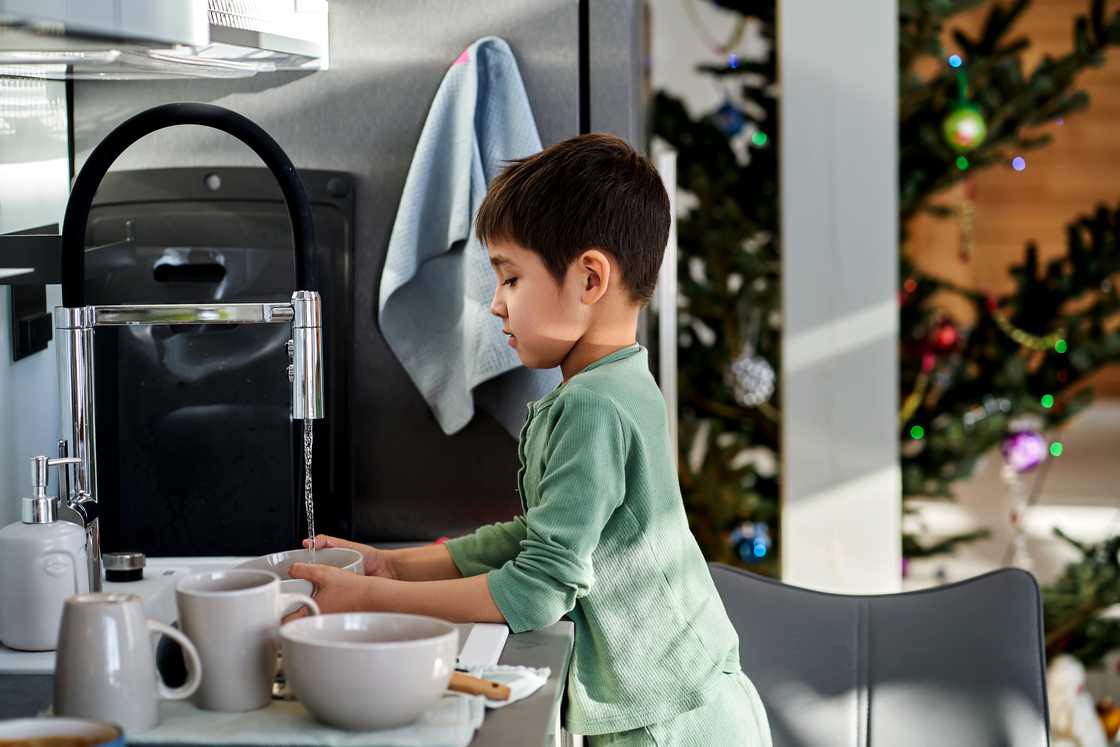 A boy washing dishes. A boy washing dishes.