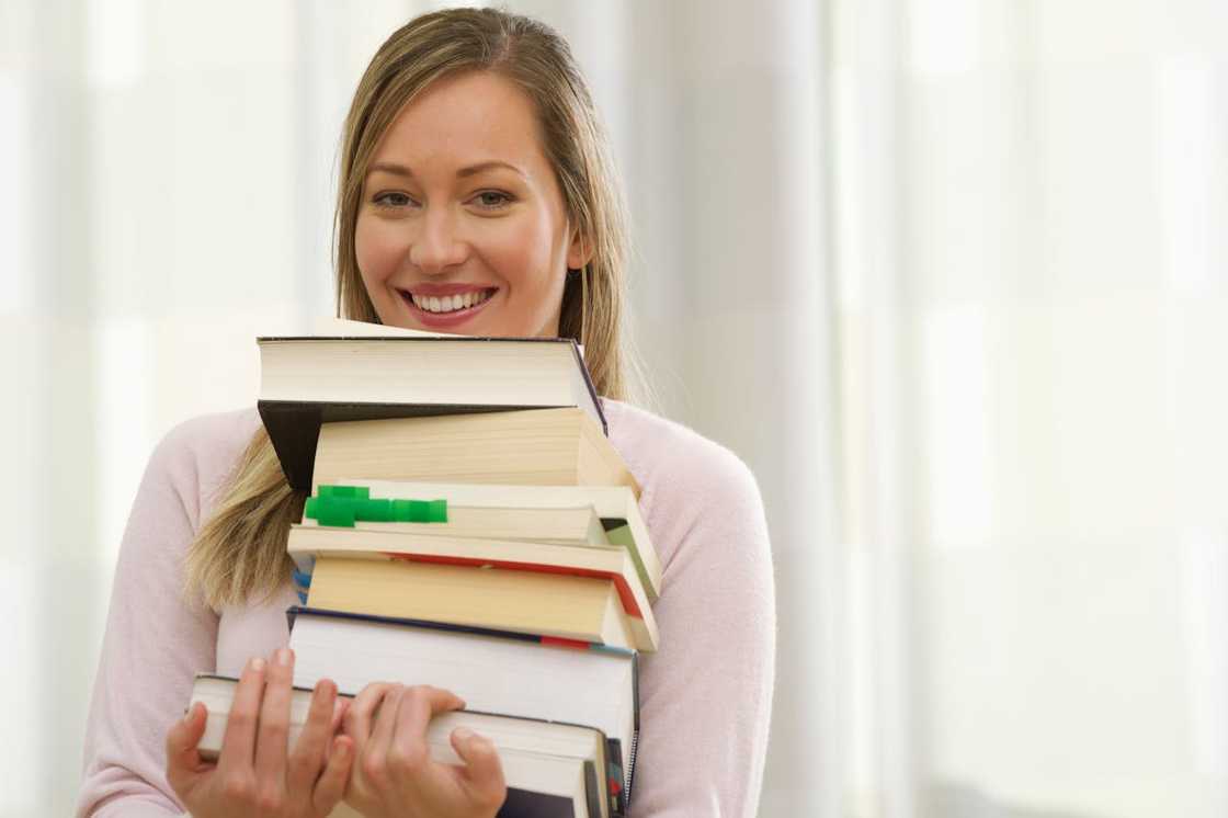 A young woman carrying a tall stack of books.