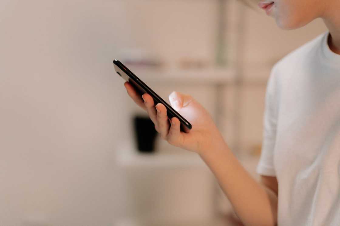 A person holds a smartphone and looks at the screen indoors.